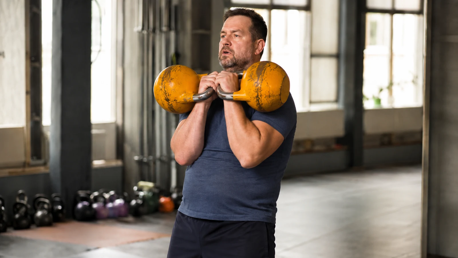 Athlet steht mit zwei Wettkampf-Kettlebells in der Rack Position und konzentriert sich auf ruhige Atmung.
