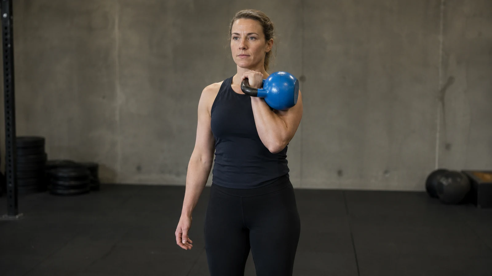 Sportlerin hält eine blaue Kettlebell kontrolliert in der Rack-Position und konzentriert sich auf saubere Technik.